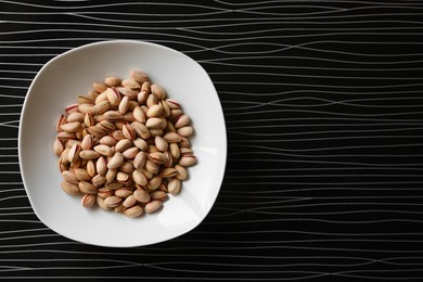 Many tasty pistachios on black table, top view. Space for text