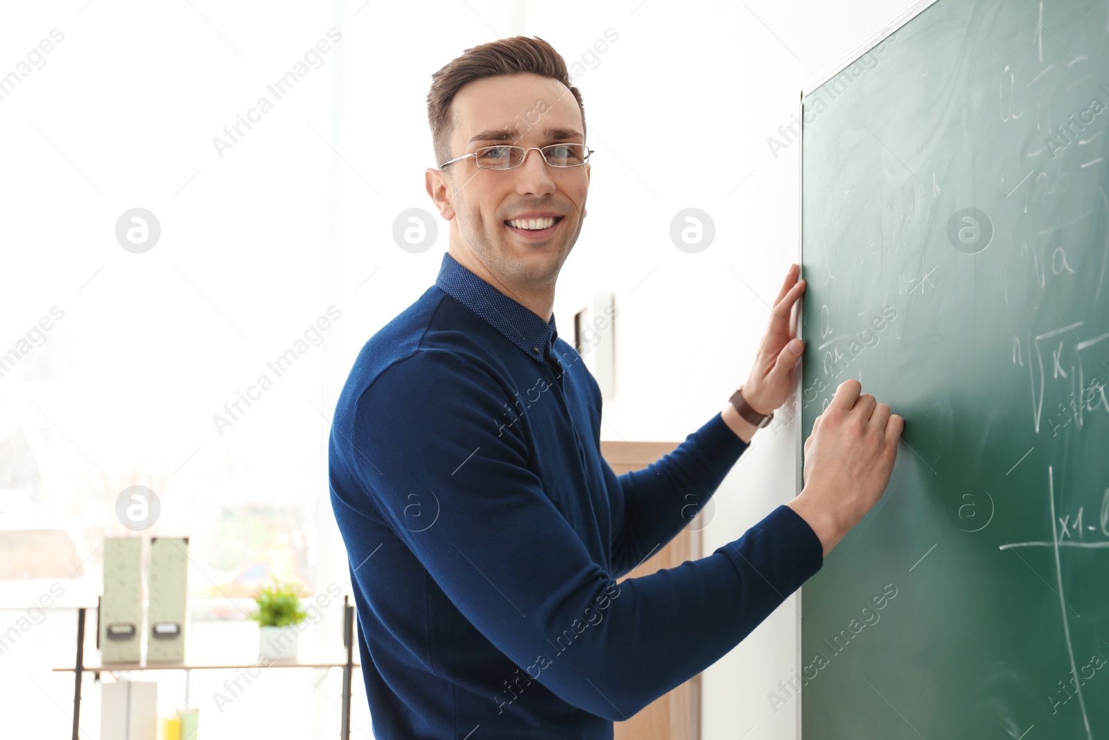 Photo of Young male teacher writing on blackboard in classroom