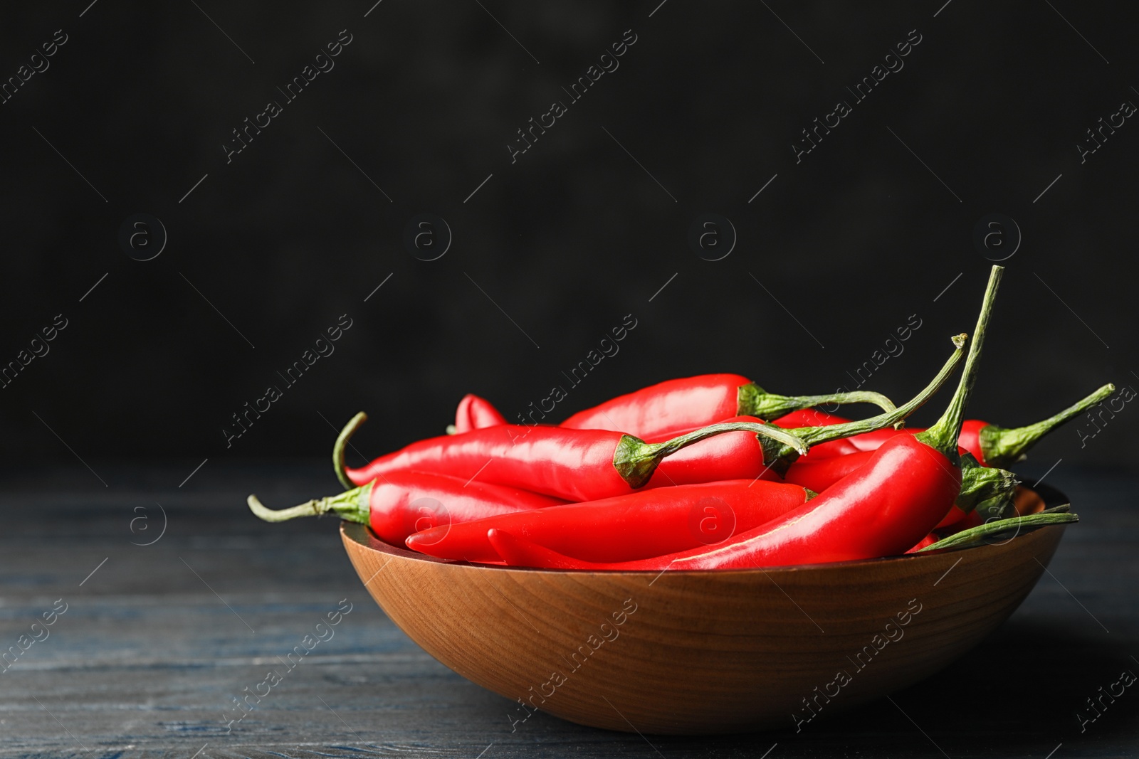 Photo of Bowl with red hot chili peppers on wooden table against black background. Space for text