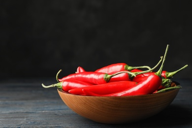 Photo of Bowl with red hot chili peppers on wooden table against black background. Space for text