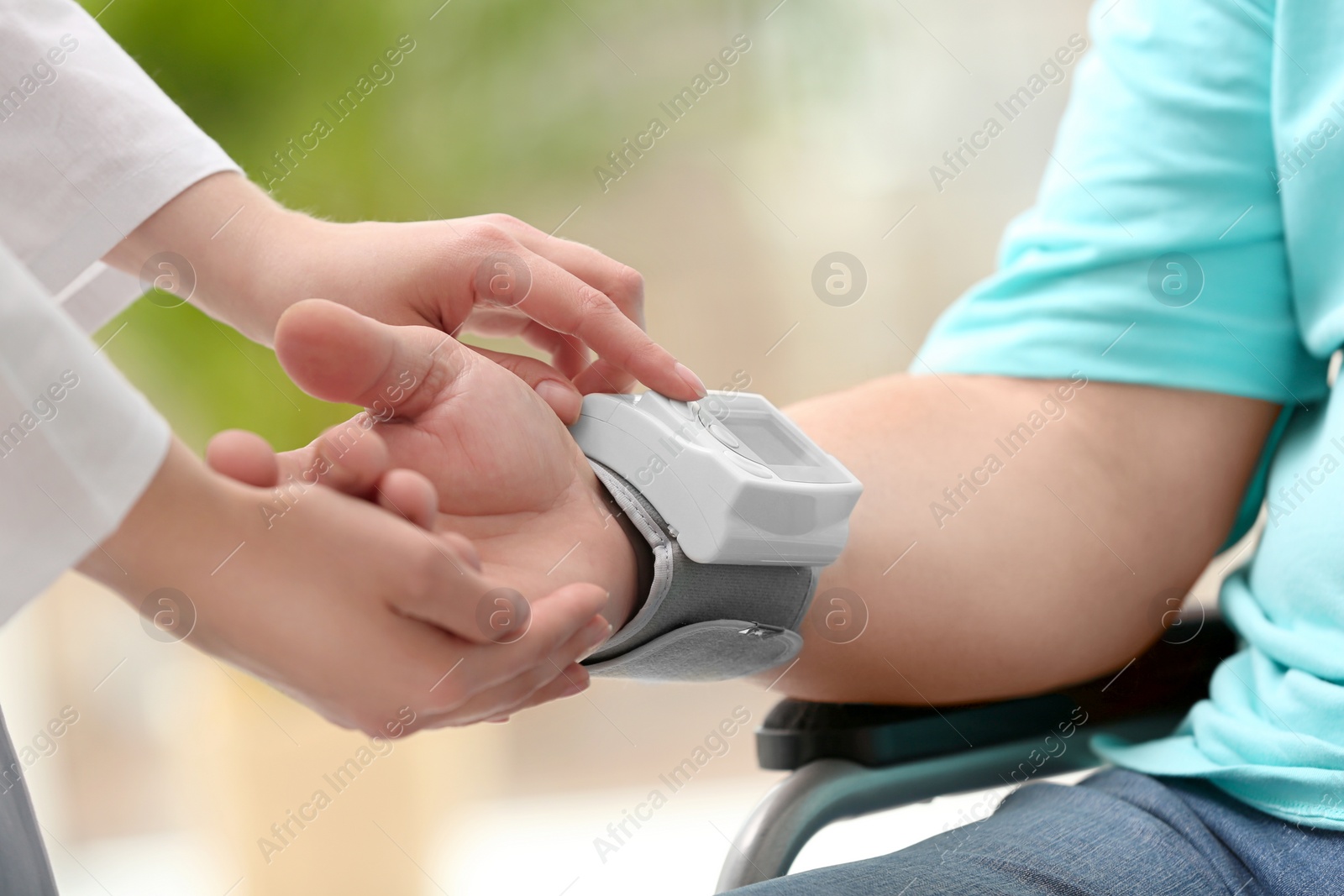 Photo of Nurse measuring blood pressure of elderly man in wheelchair against blurred background, closeup. Assisting senior generation