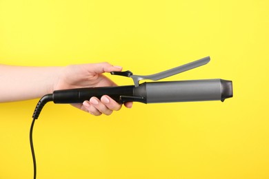 Photo of Hair styling appliance. Woman holding curling iron on yellow background, closeup