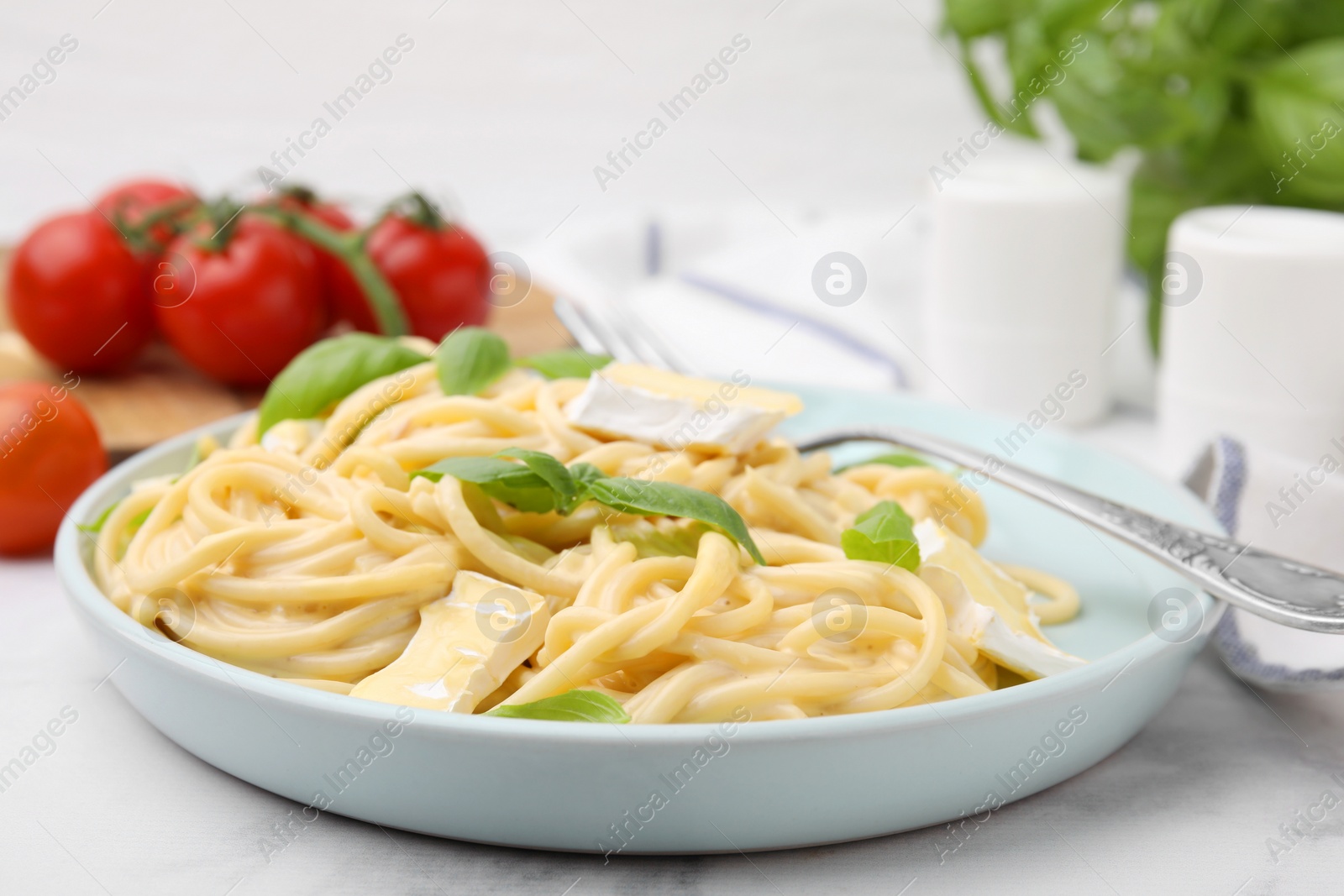 Photo of Delicious pasta with brie cheese, basil and fork on white marble table, closeup