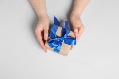 Woman holding gift box with blue bow on white background, top view