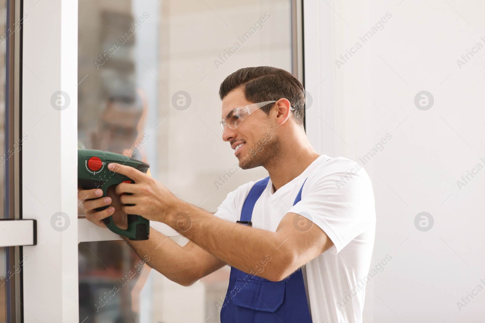 Photo of Construction worker repairing plastic window with electric screwdriver indoors