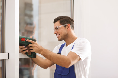 Construction worker repairing plastic window with electric screwdriver indoors