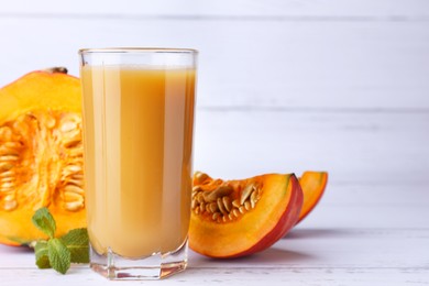 Tasty pumpkin juice in glass and cut pumpkin on white wooden table. Space for text