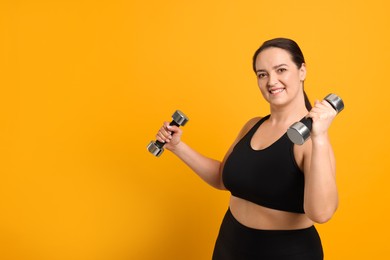 Photo of Happy overweight woman doing exercise with dumbbells on orange background, space for text