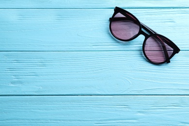 Stylish sunglasses on light blue wooden background, top view. Space for text