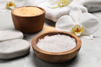 Natural sea salt in bowls, spa stones and flowers on grey marble table, closeup