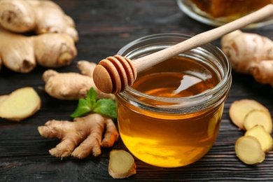 Photo of Honey and ginger on black wooden table, closeup. Natural cold remedies