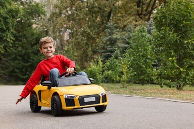 Photo of Cute little boy driving children's car outdoors. Space for text