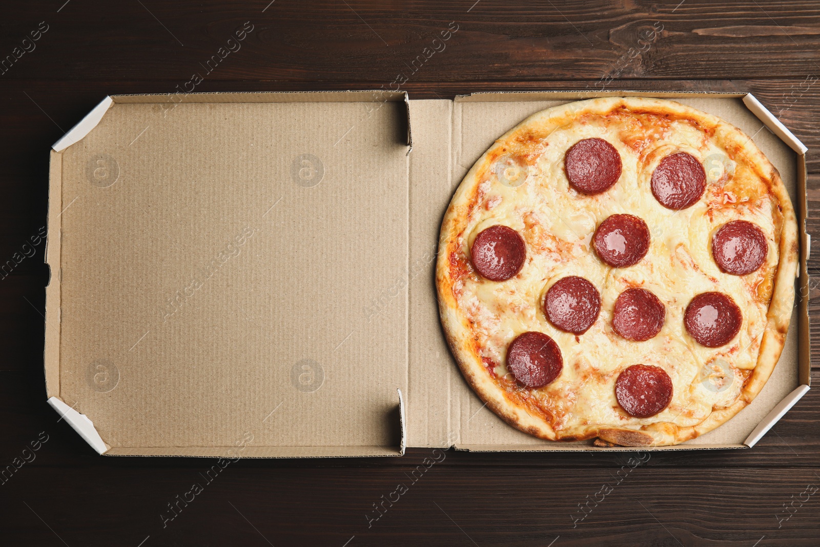 Photo of Tasty pepperoni pizza in cardboard box on wooden table, top view