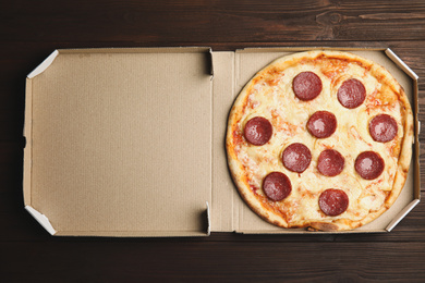 Tasty pepperoni pizza in cardboard box on wooden table, top view