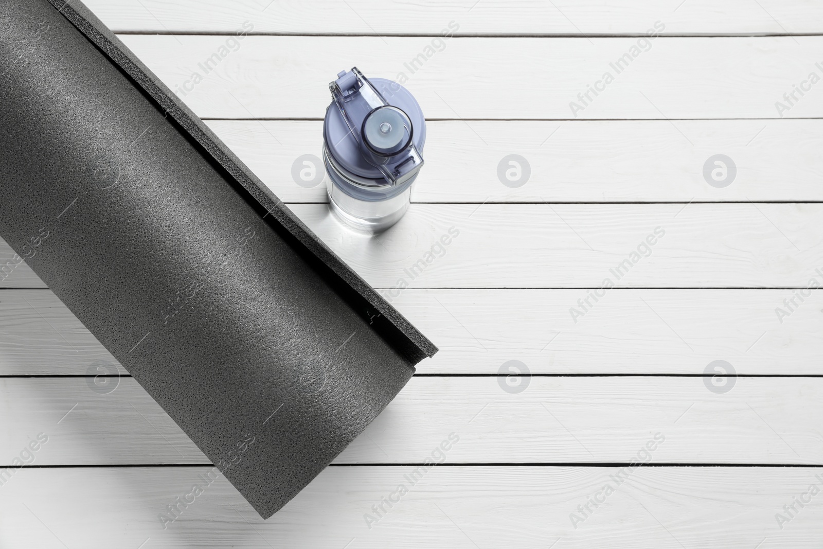 Photo of Yoga mat and bottle of water on white wooden floor, flat lay. Space for text