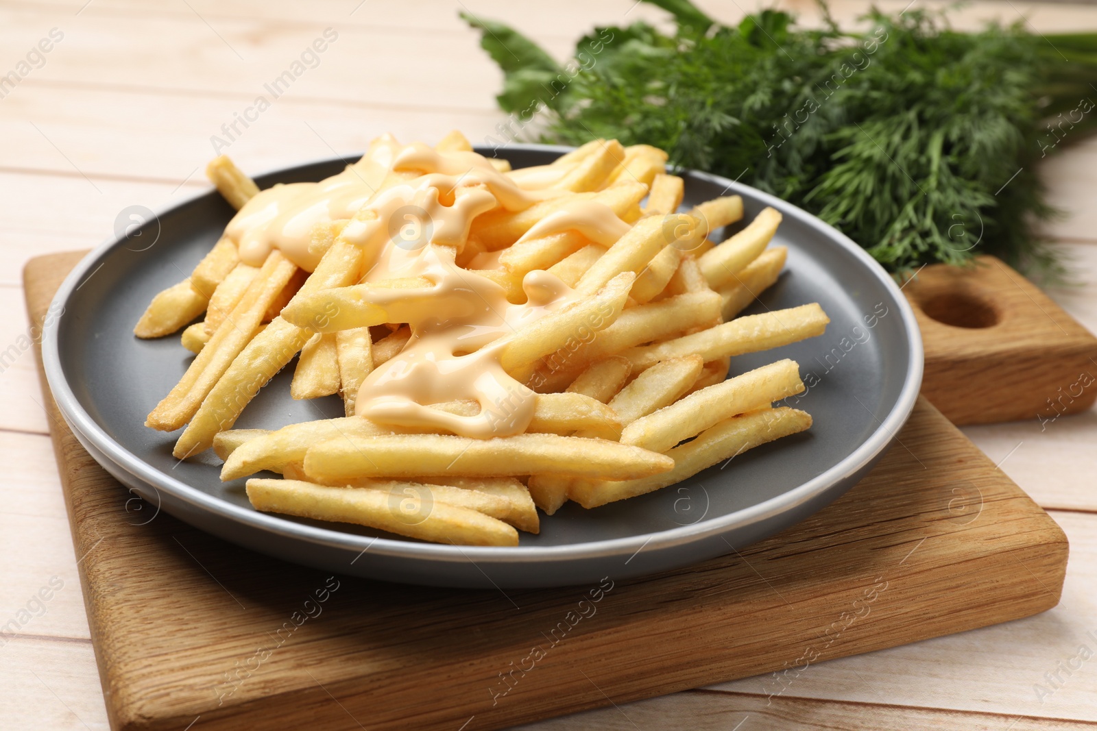 Photo of Delicious french fries with cheese sauce on wooden table, closeup