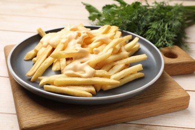 Photo of Delicious french fries with cheese sauce on wooden table, closeup