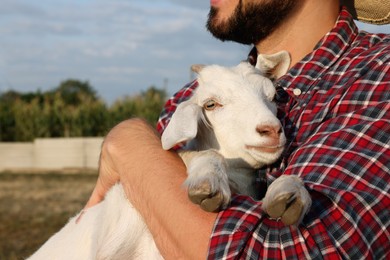Photo of Farmer with cute goatling outdoors, closeup. Baby animal