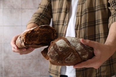 Photo of Man breaking loaf of fresh bread near grey wall, closeup