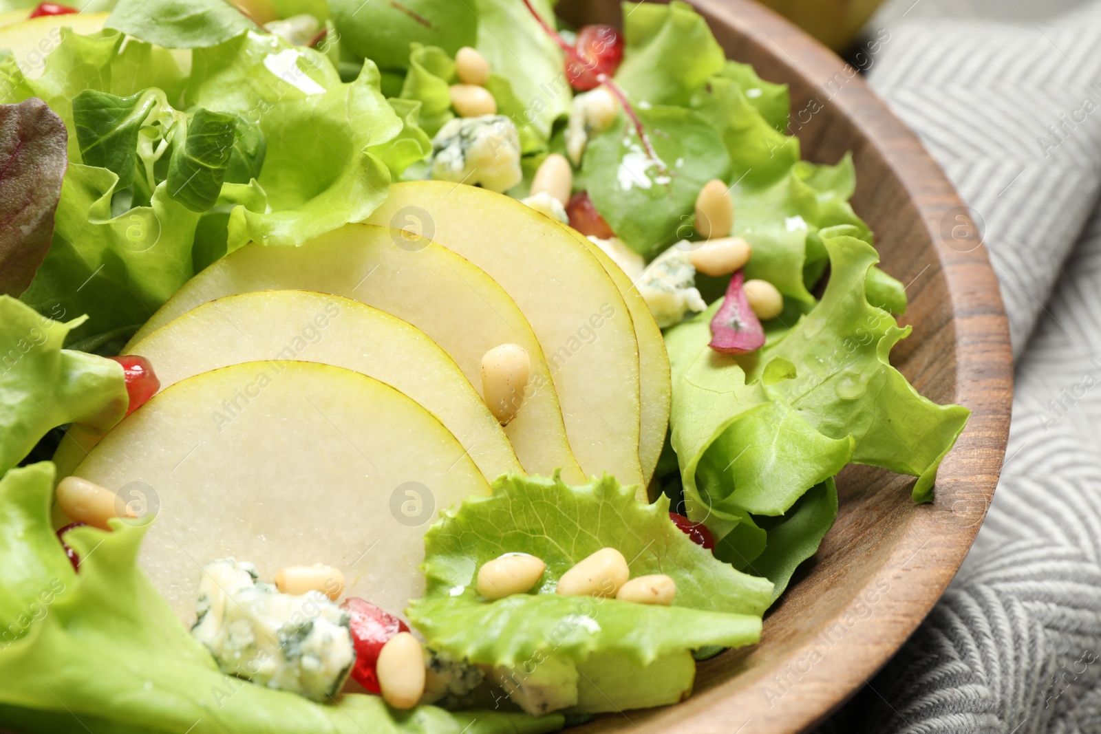 Photo of Fresh salad with pear slices in wooden bowl, closeup