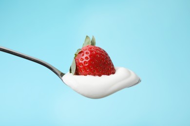 Photo of Spoon with yogurt and strawberry on light blue background, closeup