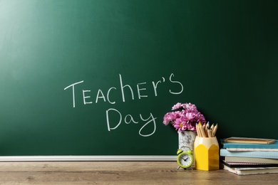 Green chalkboard with inscription TEACHER'S DAY and vase of flowers on wooden table