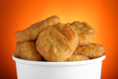 Bucket with delicious chicken nuggets on orange background, closeup