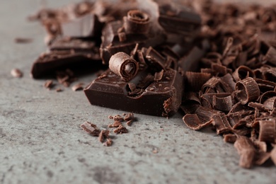 Photo of Curls and pieces of tasty chocolate on gray background, closeup