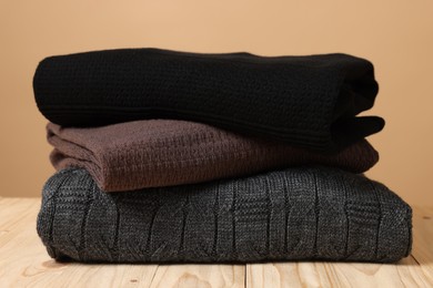 Photo of Stack of casual sweaters on wooden table against light brown background, closeup