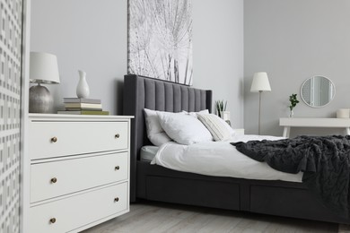 Stylish bedroom interior with large comfortable bed, chest of drawers and dressing table