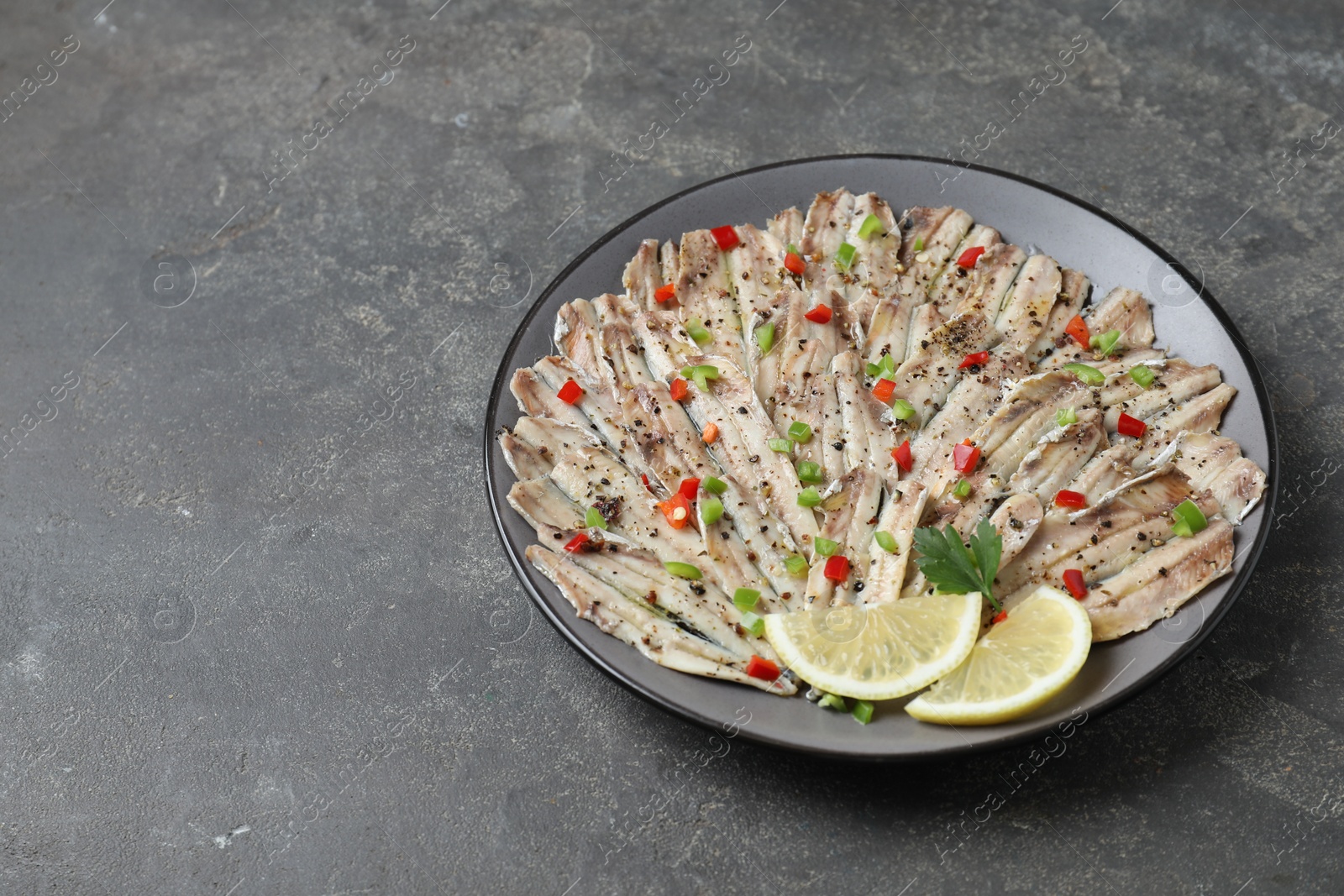 Photo of Tasty pickled anchovies with spices on grey textured table, space for text