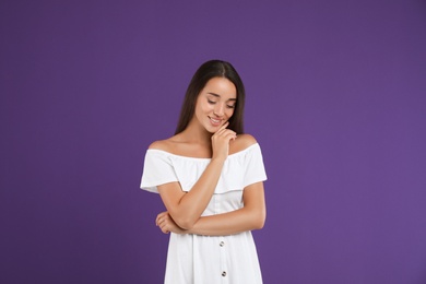 Young woman wearing stylish white dress on purple background