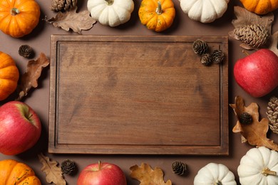 Thanksgiving day. Flat lay composition with pumpkins and wooden board on brown background, space for text