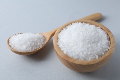 Photo of Organic white salt in bowl and spoon on light grey background, closeup