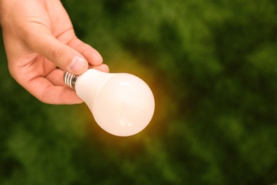 Photo of Man holding lamp bulb against green background. Space for text