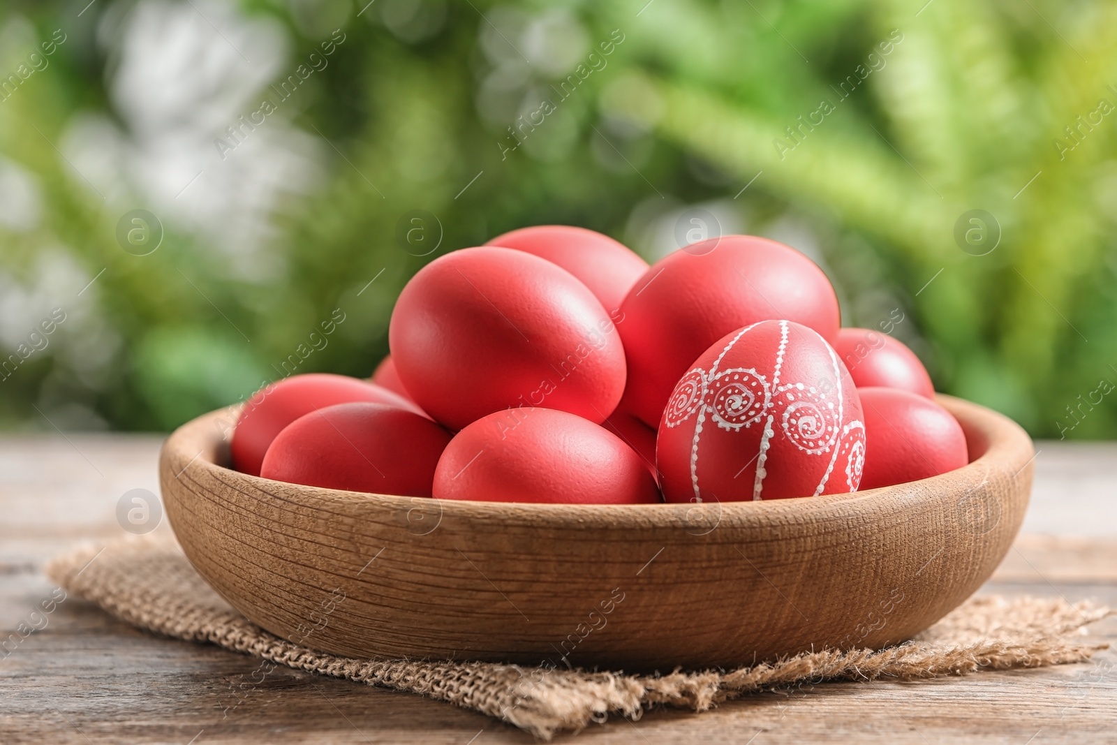 Photo of Wooden bowl with red painted Easter eggs on table against blurred background