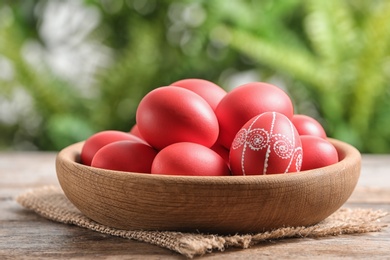 Photo of Wooden bowl with red painted Easter eggs on table against blurred background