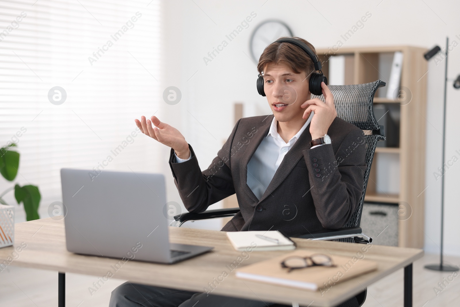 Photo of Man in headphones using video chat during webinar at wooden table in office