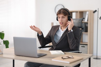 Man in headphones using video chat during webinar at wooden table in office