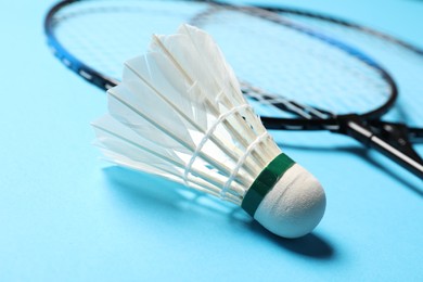 Photo of Feather badminton shuttlecock and rackets on light blue background, closeup