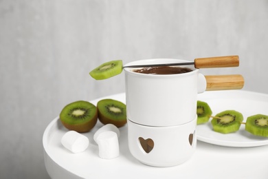 Fondue pot with chocolate and kiwi on white table