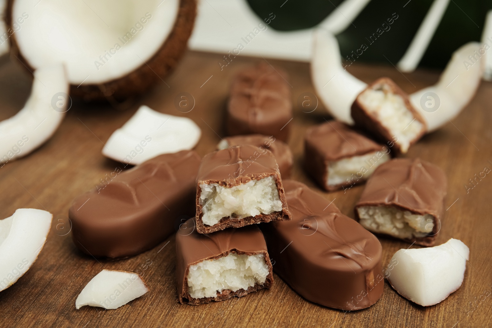 Photo of Delicious milk chocolate candy bars with coconut filling on wooden board, closeup