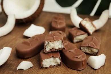 Delicious milk chocolate candy bars with coconut filling on wooden board, closeup