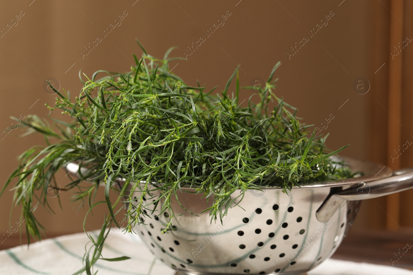 Photo of Colander with fresh tarragon leaves on table, closeup