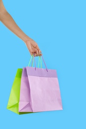 Woman with paper shopping bags on light blue background, closeup