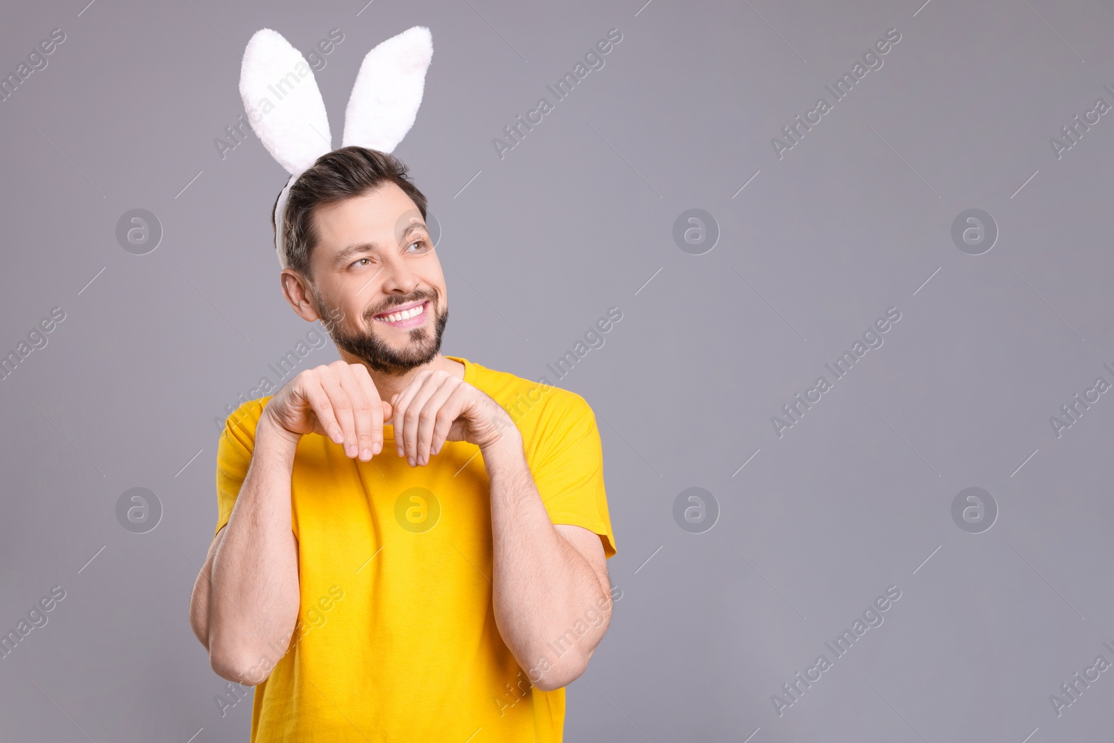 Photo of Happy man wearing bunny ears headband on grey background, space for text. Easter celebration