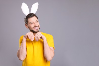 Photo of Happy man wearing bunny ears headband on grey background, space for text. Easter celebration