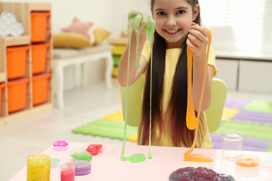 Photo of Little girl playing with slime in room