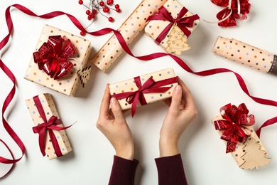 Photo of Woman holding Christmas gift box with red bow at white table, top view