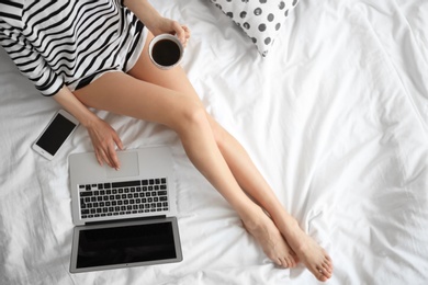 Photo of Female blogger with laptop and cup of coffee on bed, top view